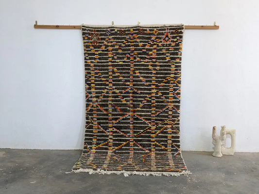 A moroccan handmade azilal rug by decorbites with dark brown base geometric patterns in orange yellow black pure natural wool