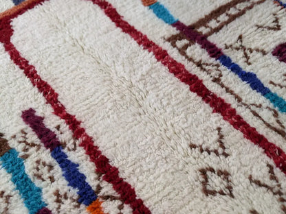 A plush white moroccan handmade traditional azilal rug with bold red blue and brown geometric patterns in thick wool