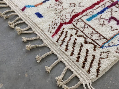Cream-colored moroccan handmade traditional azilal rug with intricate red blue brown wool patterns and fringed edge 250 x 150 cm