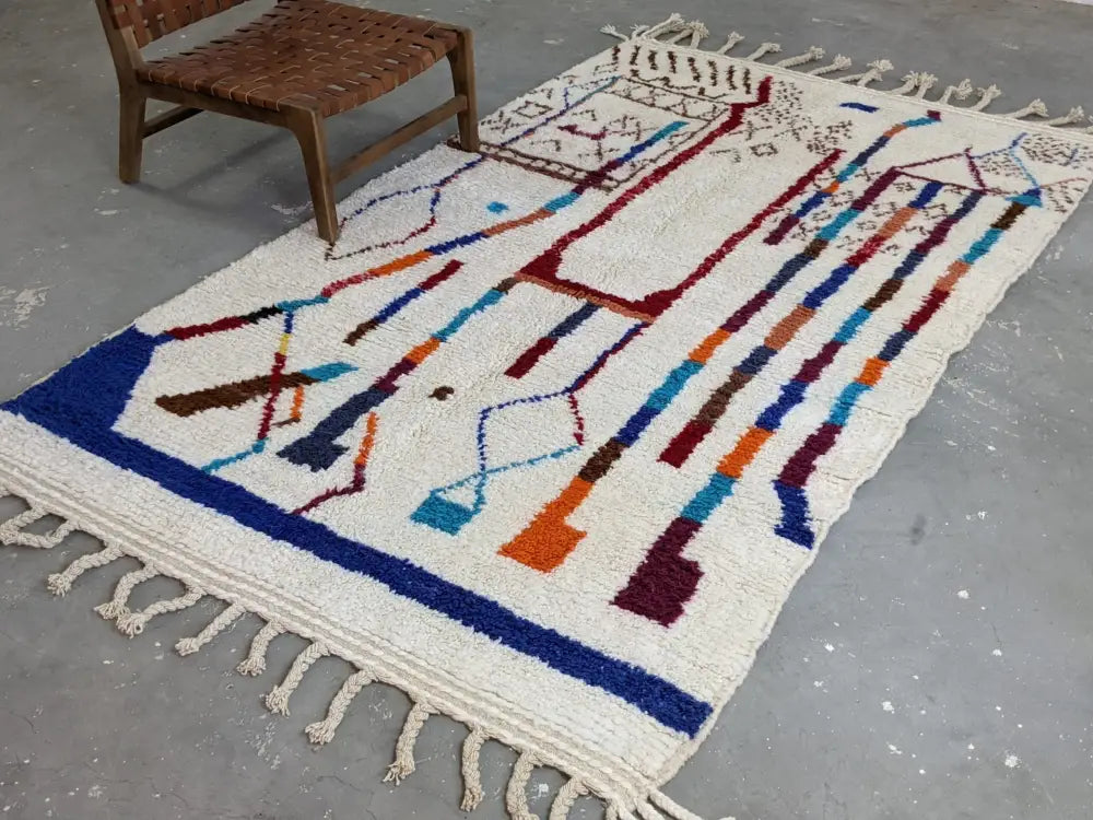 Cream-colored moroccan handmade traditional azilal rug with bold blue red orange and brown geometric patterns and fringed edges