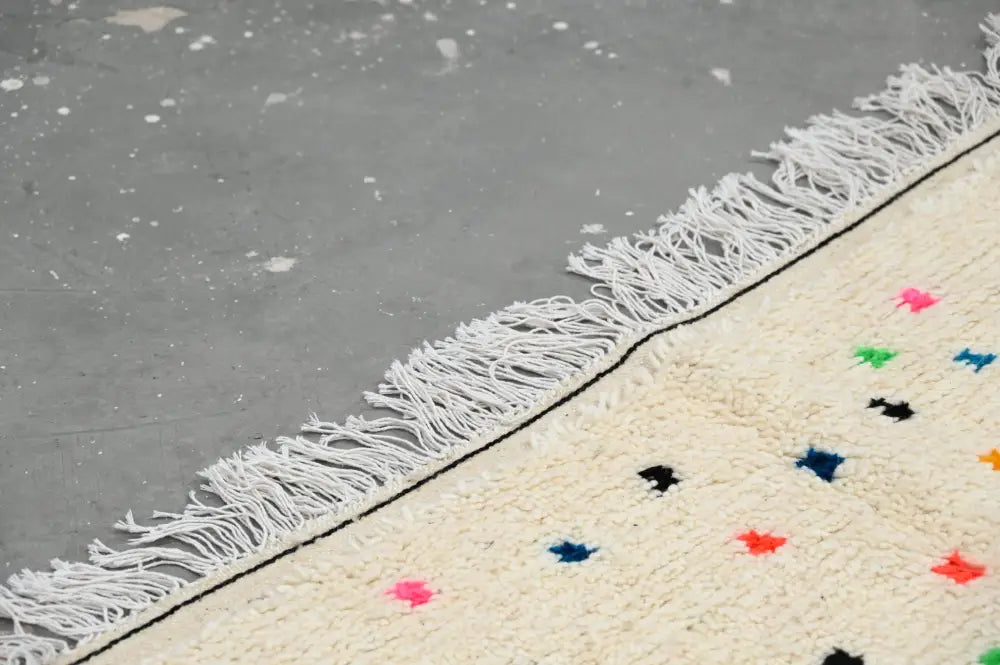 Cream-colored moroccan handmade traditional azilal rug with white fringe and colorful geometric patterns by DecorBites