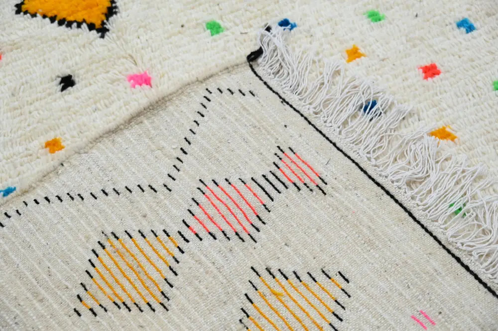 A cream-colored DecorBites™ moroccan handmade traditional Azilal rug with black orange pink and yellow geometric patterns