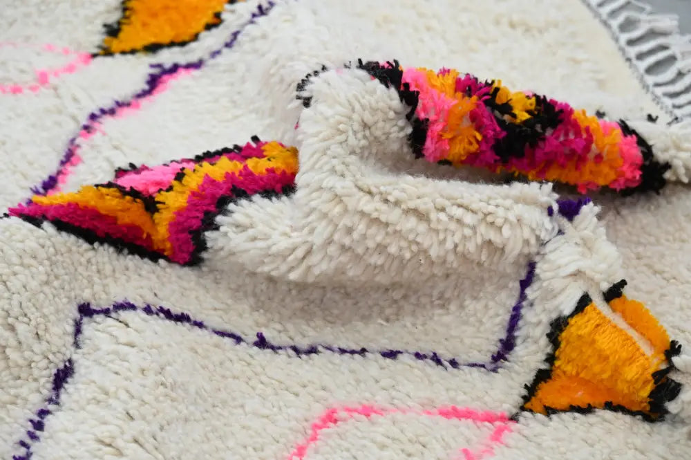 A plush cream-colored moroccan handmade traditional azilal rug with vibrant pink orange and black geometric patterns