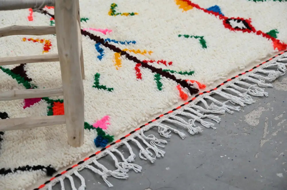 A vibrant cream-colored moroccan handmade traditional azilal rug with colorful geometric patterns and fringe border