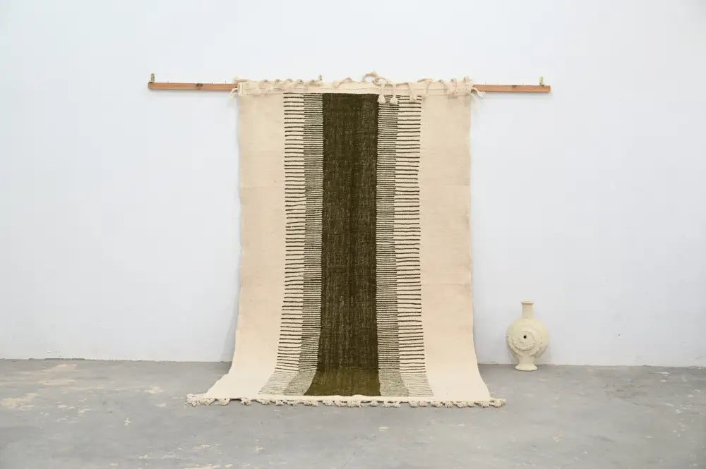 Beige and olive green moroccan handmade traditional azilal rug with woven texture and frayed edges hanging on wooden rod