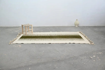 A cream-colored moroccan handmade traditional azilal rug with a central olive green stripe and fringed edges