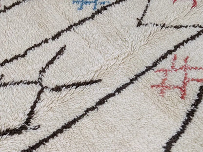 Cream-colored moroccan handmade azilal rug with plush texture bold black geometric lines and subtle blue pink details in pure natural wool