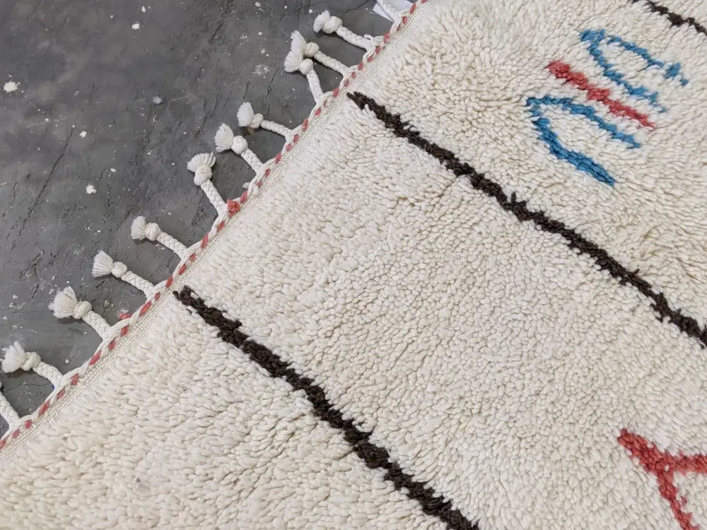 Cream-colored moroccan handmade azilal rug with black red and blue geometric patterns in pure natural wool with white tassels