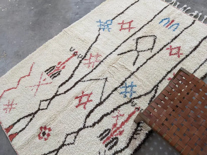Cream-colored moroccan handmade azilal rug in pure natural wool with black red and blue geometric patterns and fringed edges