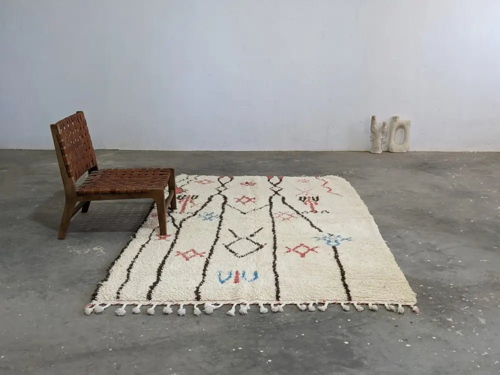 Cream-colored moroccan handmade azilal rug with intricate black red blue geometric patterns and fringed edge in pure natural wool
