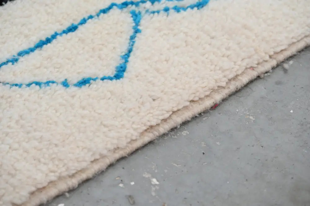 Cream-colored plush moroccan handmade traditional azilal rug with blue geometric pattern stitched along edge 254 x 143 cm