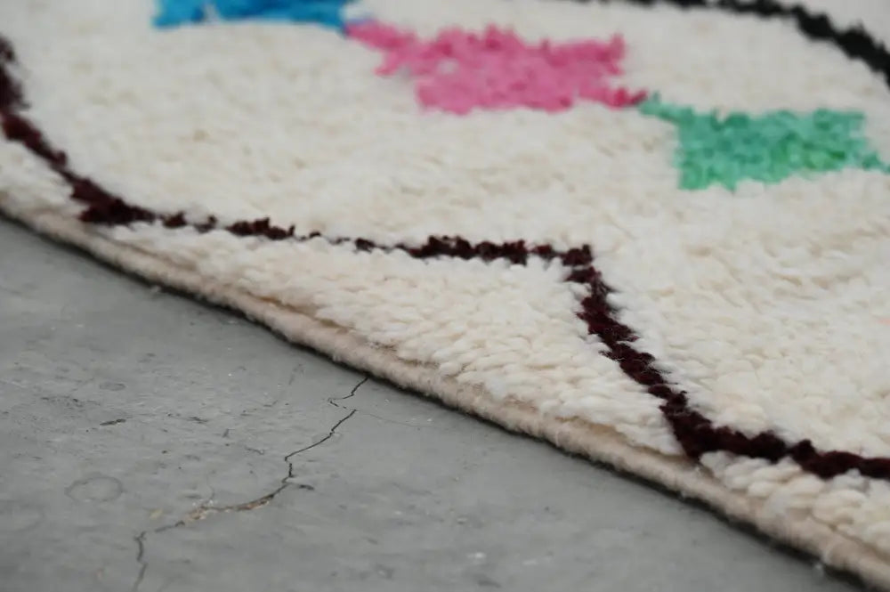 A moroccan handmade traditional azilal rug by decorbites featuring a plush white base with colorful floral patterns and dark brown fringe