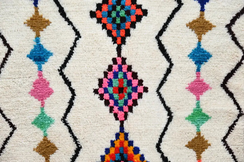 A moroccan handmade traditional azilal rug with vibrant geometric patterns in pink blue green orange and brown on white plush background