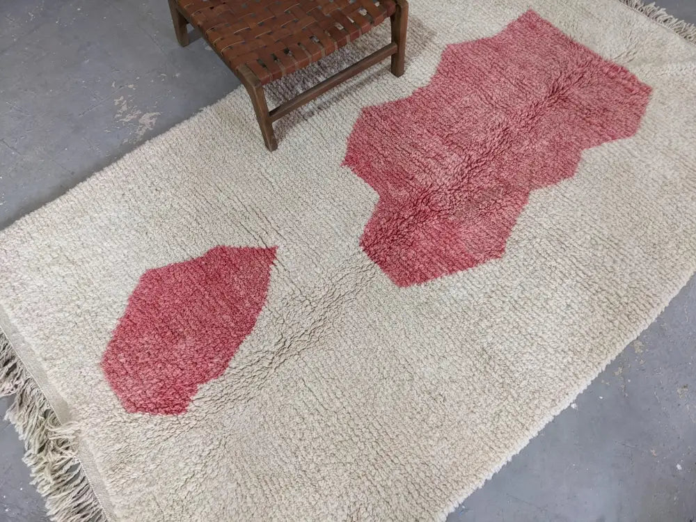 Cream-colored moroccan handmade traditional azilal rug with red textured patches and fringed edges by decorbites