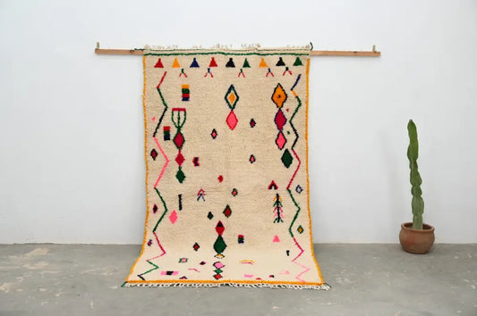 Beige moroccan handmade traditional azilal rug with vibrant pink green orange and red geometric patterns on woolen surface