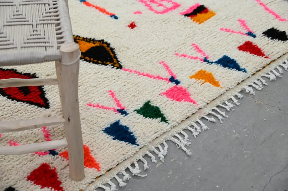 A vibrant cream-colored DecorBites™ moroccan handmade traditional azilal rug with bold pink red blue green and orange patterns