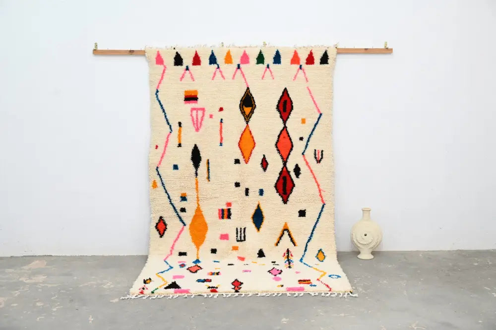 A vibrant cream-colored decorbites™ moroccan handmade traditional azilal rug with bold orange pink red and black geometric patterns