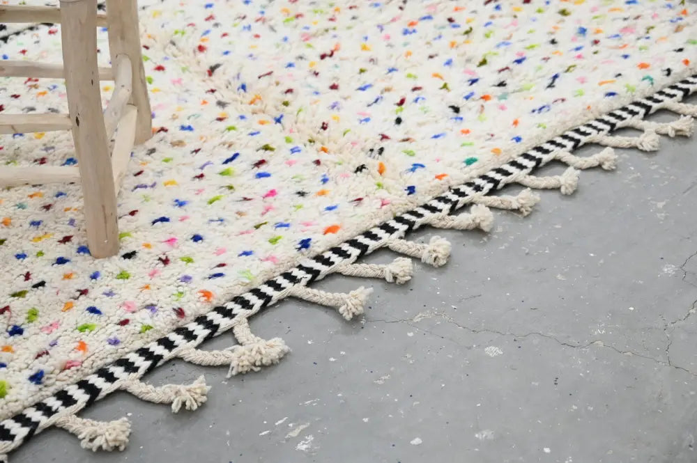 Cream-colored moroccan handmade traditional azilal rug with vibrant multicolored speckles and black-and-white striped tassel border