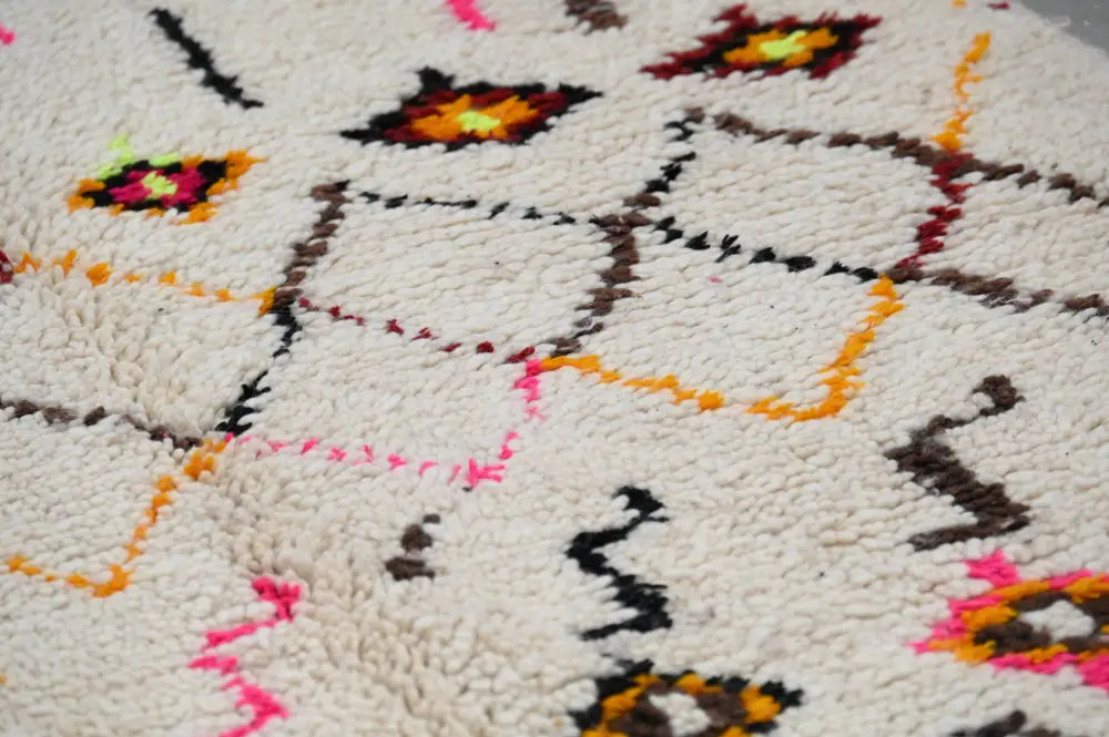 A plush off-white moroccan handmade traditional azilal rug with vibrant orange pink black and brown geometric patterns