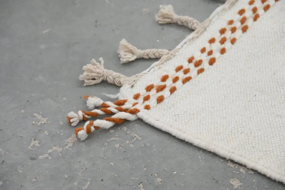 A cream-colored moroccan handmade traditional azilal rug with rust-orange dotted border and matching tassels 258 x 143 cm
