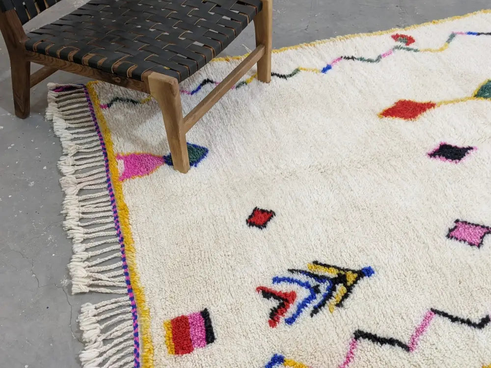 A vibrant cream-colored moroccan handmade traditional azilal rug with colorful geometric patterns and fringed edges