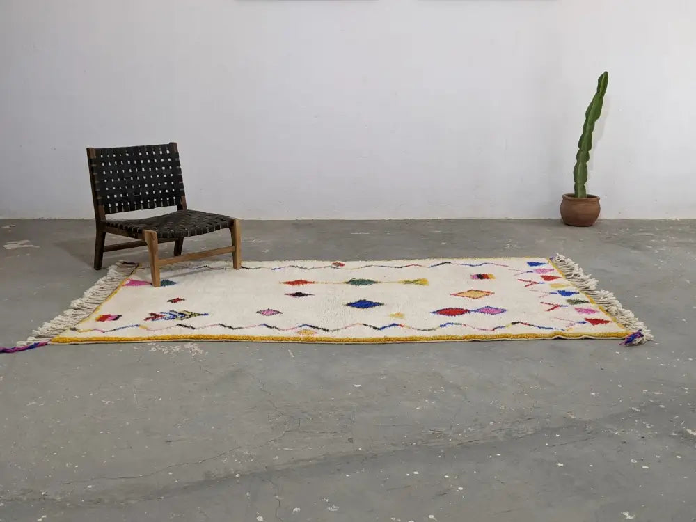 A cream-colored moroccan handmade traditional azilal rug with colorful geometric patterns and fringed edges by DecorBites