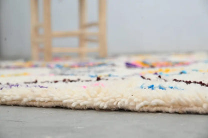 A cream-colored moroccan handmade traditional azilal rug with vibrant geometric patterns and thick textured fringe