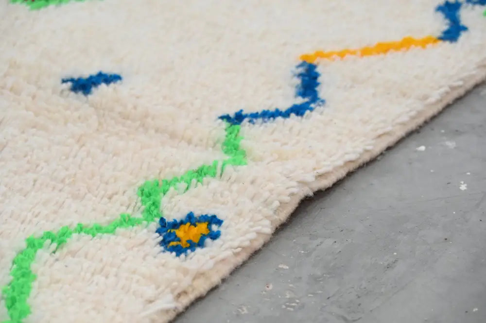 Cream-colored plush wool moroccan handmade traditional azilal rug with vibrant blue green and yellow zigzag patterns