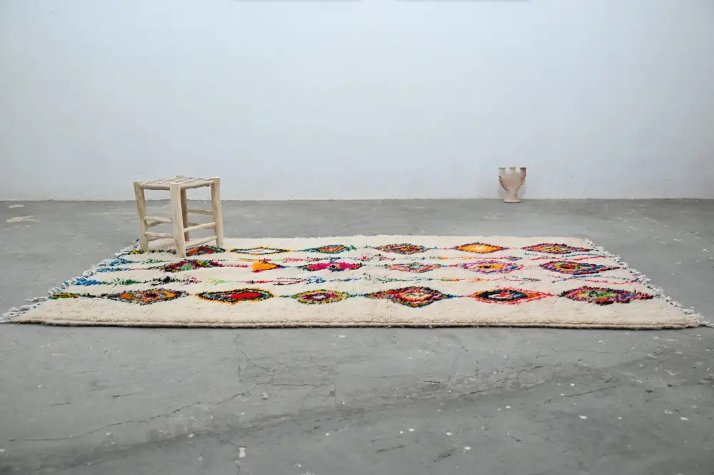 A cream-colored DecorBites™ moroccan handmade traditional azilal rug with vibrant geometric patterns and fringed edges