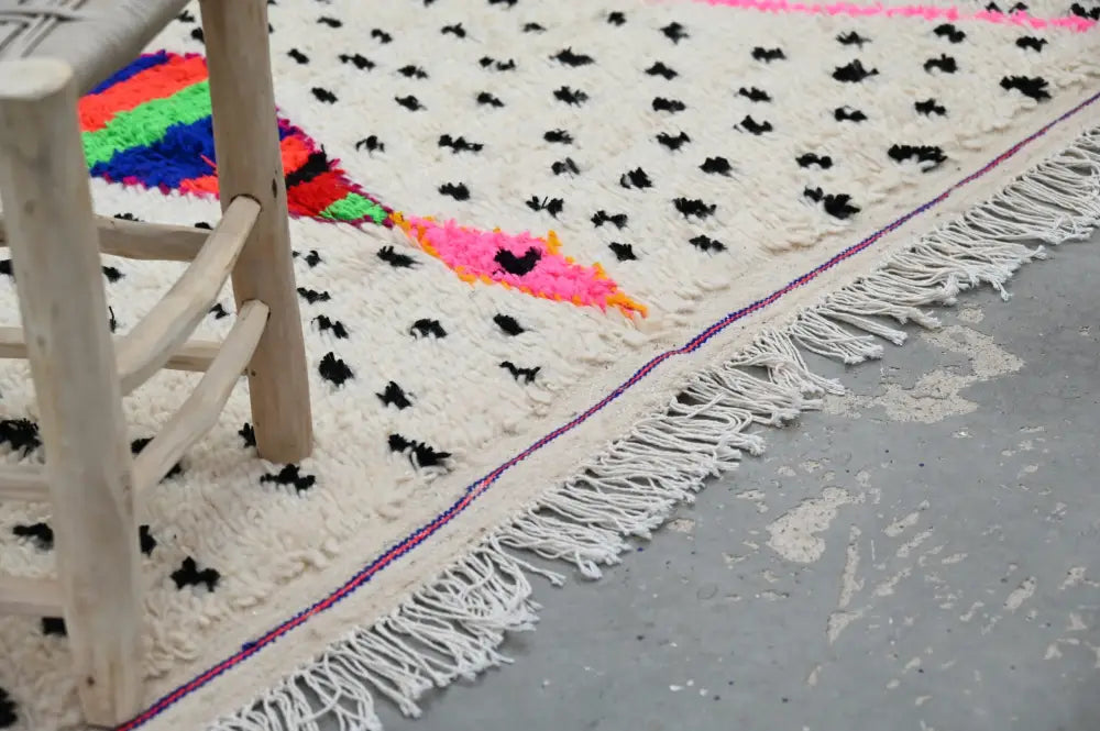 A cream-colored moroccan handmade traditional azilal rug with black embroidery and multicolored geometric edge pattern