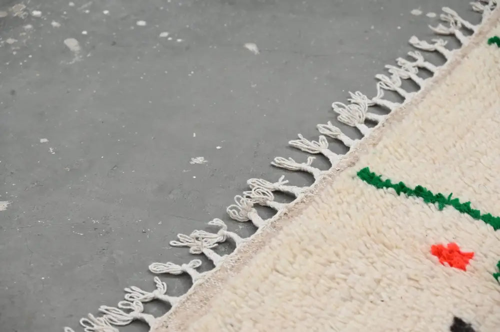 Cream-colored wool moroccan handmade traditional azilal rug with fringed edges and bold green and red geometric patterns