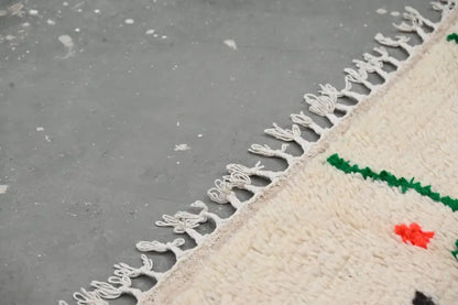 Cream-colored wool moroccan handmade traditional azilal rug with fringed edges and bold green and red geometric patterns
