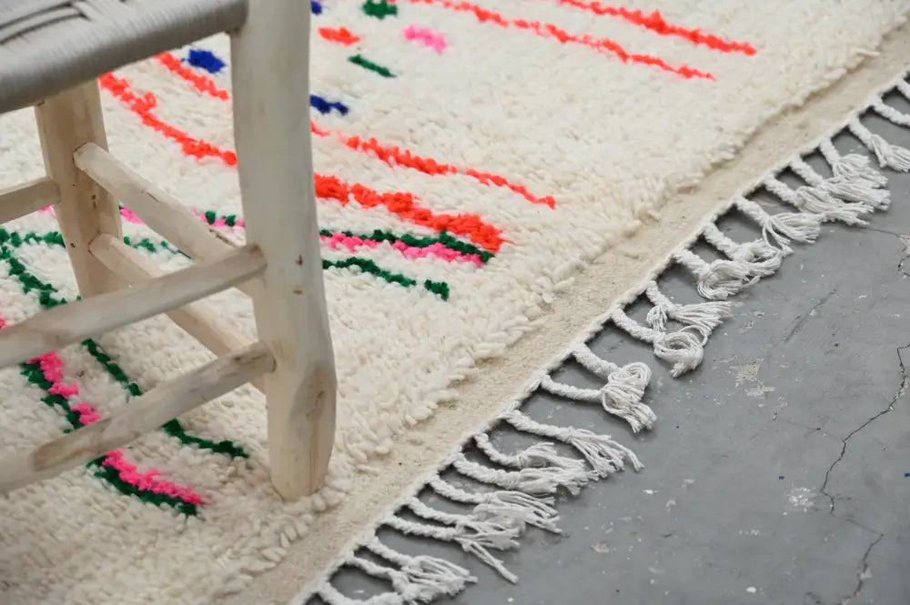 Cream-colored moroccan handmade traditional azilal rug with vibrant red pink green geometric patterns and fringed edge