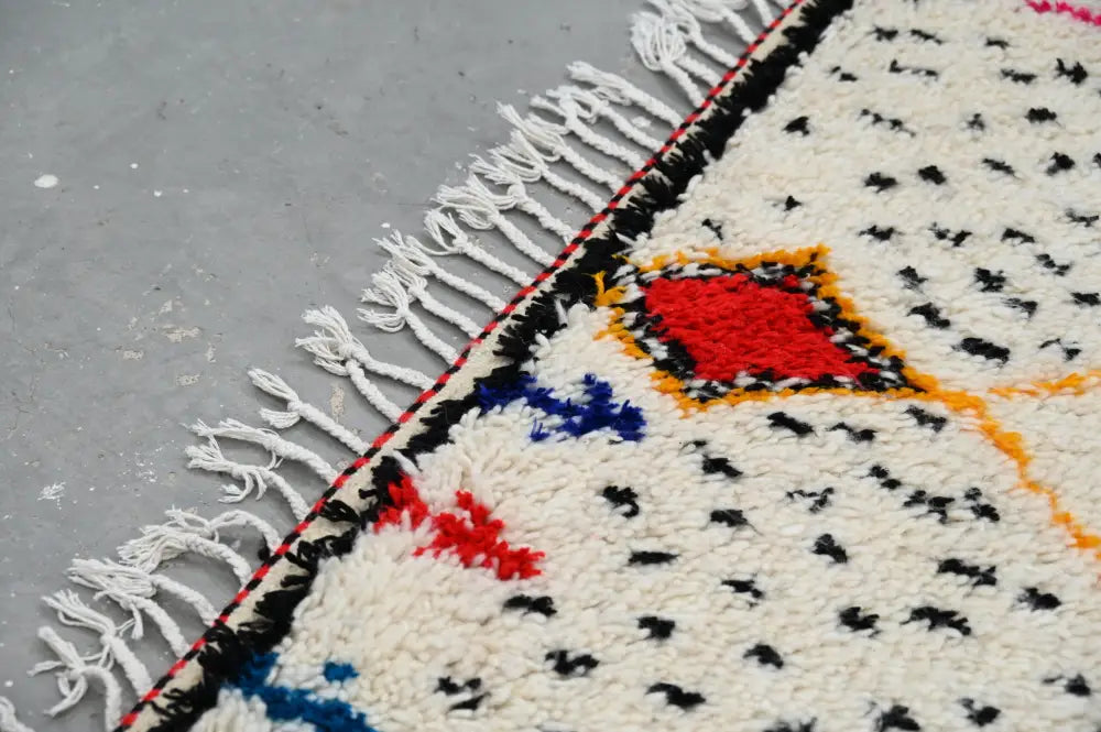 Cream-colored moroccan handmade traditional azilal rug with bold red blue black geometric patterns and white fringe border