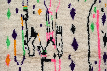 A cream-colored moroccan handmade traditional azilal rug with vibrant geometric patterns in purple green pink orange and black