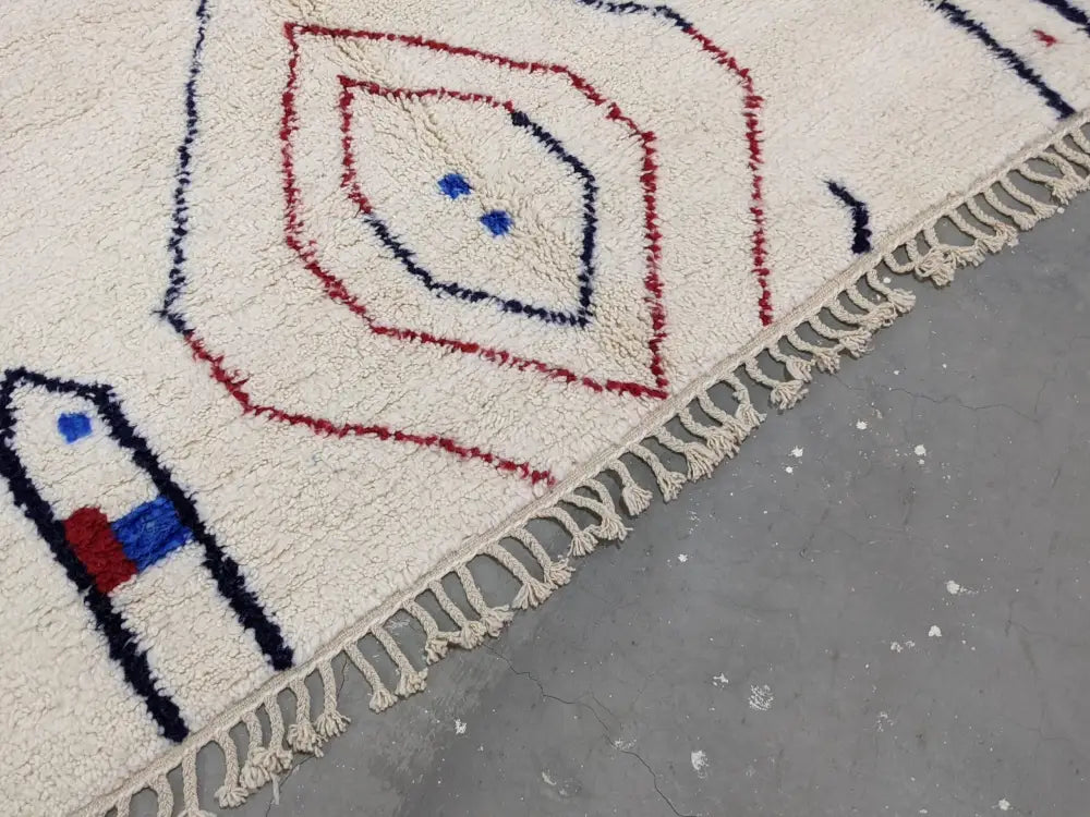 Cream-colored moroccan handmade traditional azilal rug with red blue and black geometric woolen patterns and fringed edge