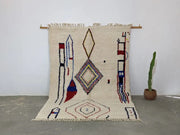 Cream-colored moroccan handmade traditional azilal rug with red blue and brown geometric patterns on woolen surface