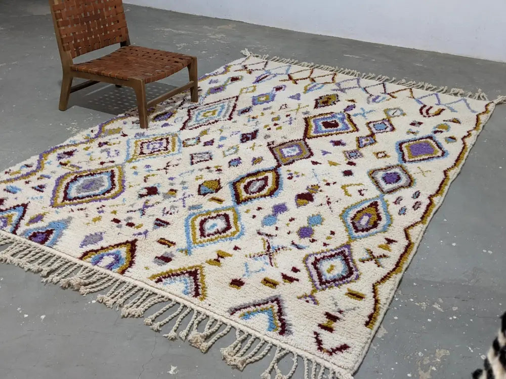 Cream-colored moroccan handmade traditional azilal rug with intricate purple blue brown geometric patterns and fringed edges