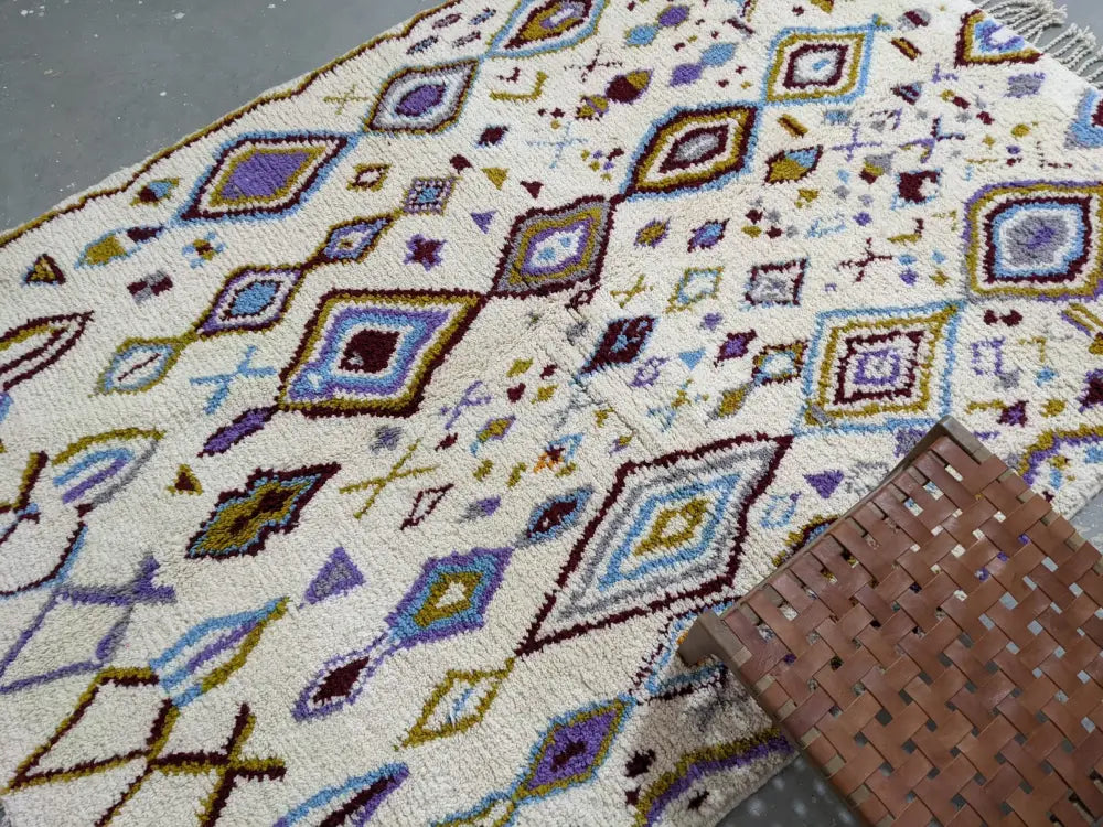 A cream-colored DecorBites™ moroccan handmade traditional Azilal rug with purple blue brown and green geometric patterns