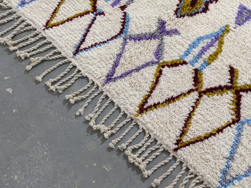 Cream-colored decorbites™ moroccan handmade traditional azilal rug with intricate purple blue mustard geometric patterns and fringe