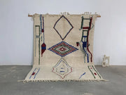 Cream-colored moroccan handmade traditional azilal rug with blue red green and black geometric patterns on woolen surface