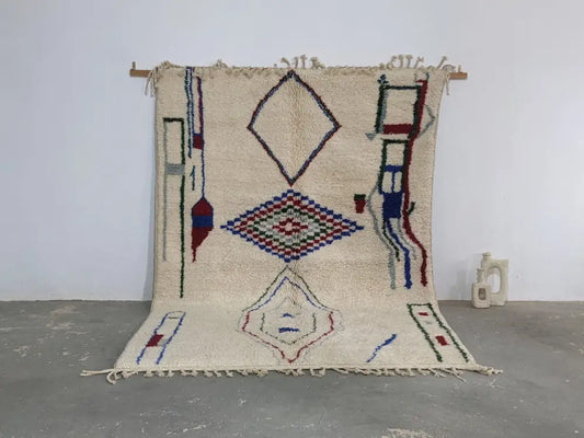 Cream-colored moroccan handmade traditional azilal rug with blue red green and black geometric patterns on woolen surface