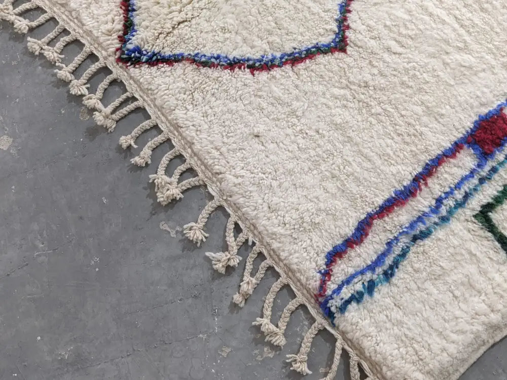 Cream-colored moroccan handmade traditional azilal rug with blue red and green geometric patterns and fringed edges