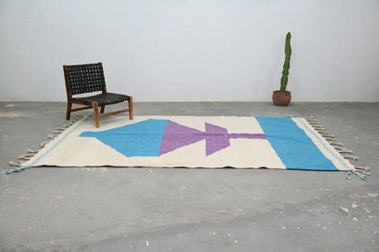 A cream-colored moroccan handmade traditional azilal rug with bold blue and purple geometric patterns and fringed edges