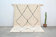 Cream-colored beni ouarain carpet with black geometric diamond patterns and fringed edges moroccan handmade rug