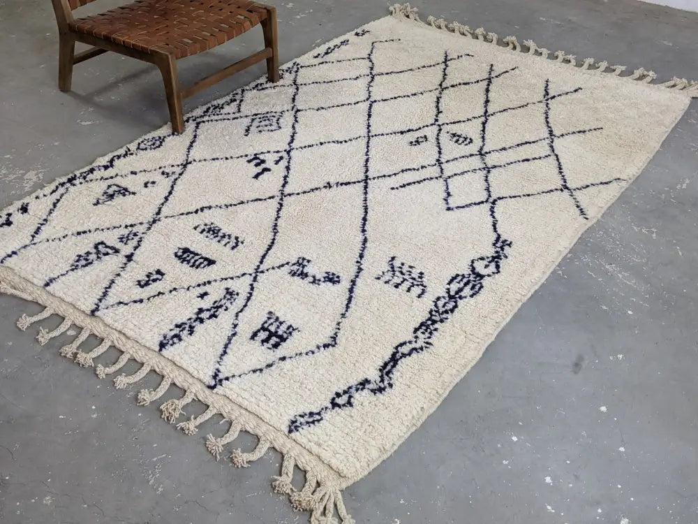 Cream-colored beni ouarain rug featuring black geometric patterns and fringed edges in moroccan handmade style
