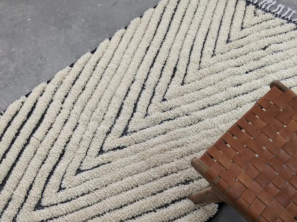 Cream-colored moroccan handmade beni ouarain rug with bold black zigzag patterns and fringed edge by DecorBites