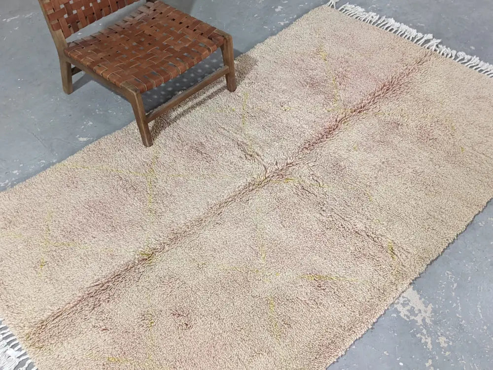 A soft beige and pinkish wool beni ouarain rug with textured shaggy surface and white fringe edges by DecorBites