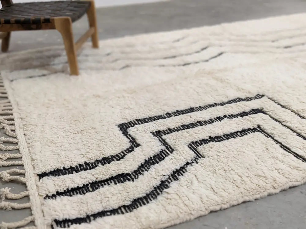 Cream-colored plush wool moroccan handmade beni ouarain rug with bold black geometric patterns and fringed edges