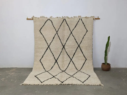 Cream-colored beni ouarain rug with black geometric diamond patterns and fringed edges moroccan handmade traditional design